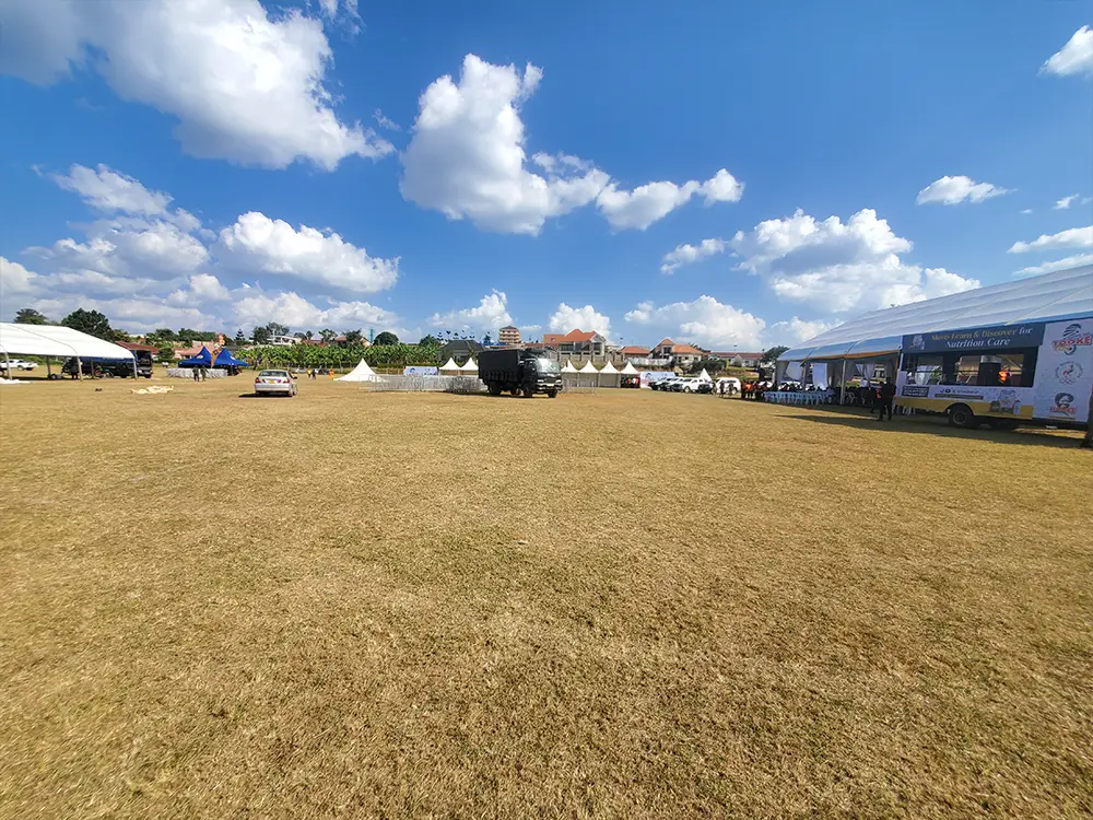 Tents and event-ground background — Bushenyi event-ground view showing tents, stage context and the physical branding environment before final setup.