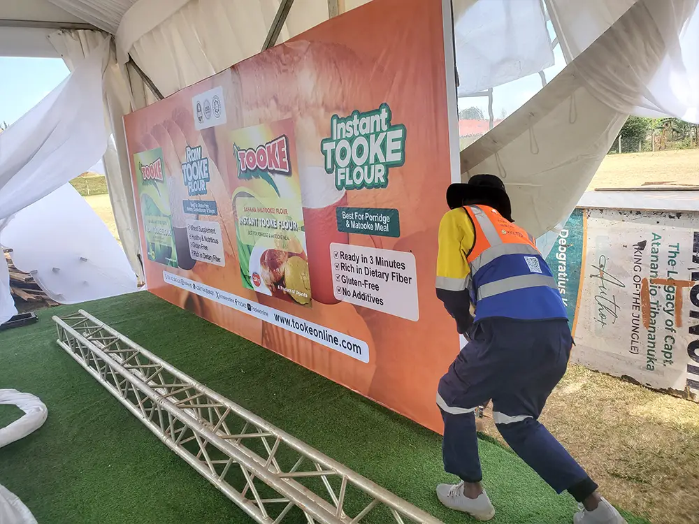 Raw Tooke Flour backdrop fixing — PVC being aligned, stretched and fixed on the VIP tent structure during the physical setup.