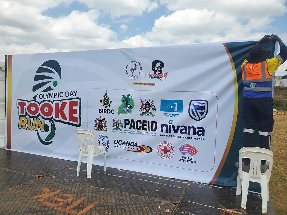 PVC fitting on outdoor media wall — Sponsor PVC being installed on the outdoor photo backdrop structure at the Bushenyi event ground.